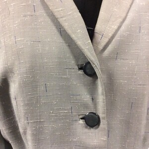 May include: A close-up of a grey blazer with a textured fabric. The blazer has two black buttons.