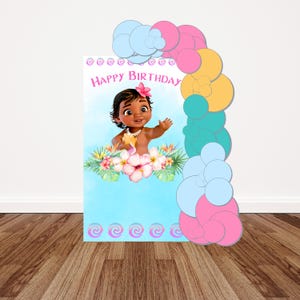 May include: A rectangular birthday sign featuring a cartoon baby with dark hair and a pink flower, surrounded by tropical flowers and leaves. The text reads Happy Birthday in pink. A balloon arch in blue, pink, yellow, and teal frames the right side.