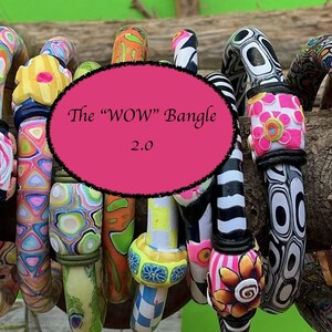 May include: A collection of colorful, patterned bangles. The bangles feature a variety of designs, including swirls, flowers, and geometric shapes. The text "The "WOW" Bangle 2.0" is displayed on a pink oval in the center of the image.