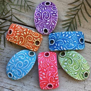 Può includere: Sei piastrelle in ceramica con un motivo floreale bianco su sfondi di vari colori. Le piastrelle sono di forma ovale e rettangolare e hanno due fori per l'appeso.