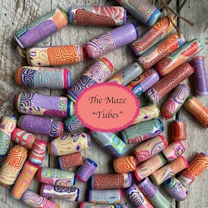 May include: A collection of colorful polymer clay tubes with swirled patterns in shades of purple, orange, red, and blue. The tubes are cylindrical and have a glossy finish. The text "The Maze 'Tubes'" is in a pink oval.