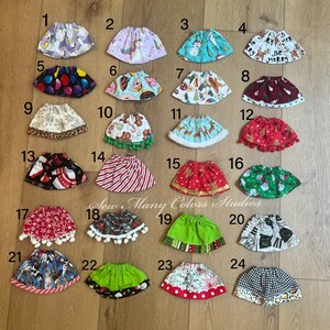 May include: A collection of twenty-four colorful, patterned skirts. Designs include unicorns, snowmen, Christmas themes, and various prints. The skirts are arranged on a wooden surface, showcasing a variety of styles and patterns.