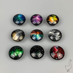 Op de afbeelding: Negen ronde, kleurrijke harsknoppen met galaxy-geïnspireerde ontwerpen. Elke knop heeft een uniek, draaiend patroon van kleuren, waaronder blauw, groen, rood, geel en wit.