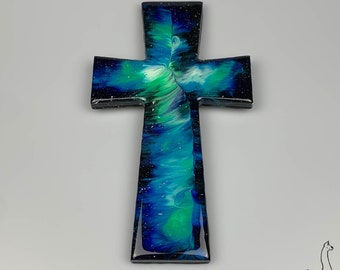 May include: A wooden cross painted with blue, green, and white abstract swirls. The cross has a black background with white speckles.