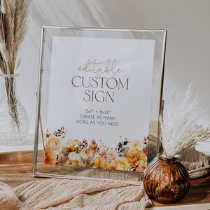 May include: A clear glass frame displays a white sign with gold script reading "editable CUSTOM SIGN". The sign has floral and pumpkin illustrations in yellow, orange, and brown. The sign is 12.7cm x 17.8cm and 20.3cm x 25.4cm.