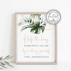 May include: A framed print with a light wood frame. The print features a watercolor design of green tropical leaves and gold accents. Gold script reads "Help the busy PARENTS-TO-BE by making yourself THE ADDRESSEE."