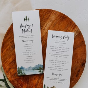 May include: A wedding ceremony program and wedding party information card with a watercolor illustration of mountains and trees. The program lists the order of the ceremony, including the prelude, processional, welcome, message, exchange of vows, exchange of rings, ceremony, blessing, pronouncement, and recessional. The wedding party information card lists the officiant, mother of the bride, father of the bride, maid of honor, bridesmaids, mother of the groom, father of the groom, best man, and groomsmen.