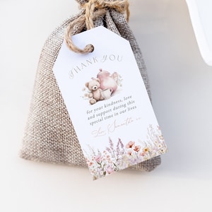 Puede incluir: Una pequeña bolsa de arpillera con una etiqueta de agradecimiento adjunta. La etiqueta presenta una ilustración de acuarela de un osito de peluche y una tetera con el texto "GRACIAS por su amabilidad, amor y apoyo durante este tiempo especial en nuestras vidas".