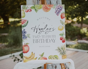 May include: Welcome to Hayley's Two-tti Frutti Birthday party sign with a watercolor design of fruit, including strawberries, blueberries, bananas, kiwi, apples, and pineapple. The sign is on a wooden easel.