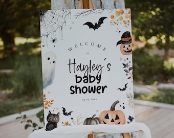May include: A white welcome sign with black text that reads "Welcome to Hayley's Baby Shower 04.03.20XX". The sign is decorated with a ghost, a black cat, bats, pumpkins, and stars.