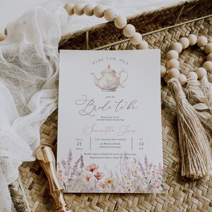 May include: A white bridal shower invitation with a watercolor floral border. The invitation features a teapot illustration and the text "Time for Tea with the Bride-to-be". The invitation also includes the bride-to-be's name, the date, time, and location of the shower.