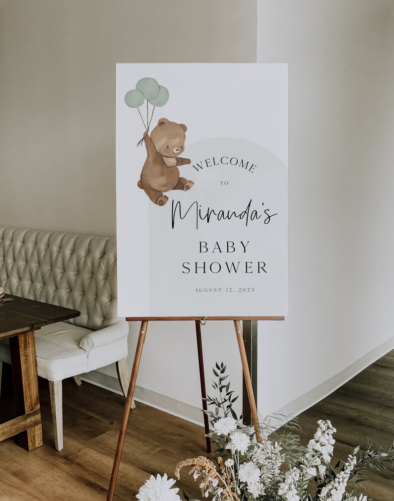 Puede incluir: Un cartel de bienvenida para un baby shower con un oso marr&oacute;n sosteniendo globos. El cartel dice "Bienvenido a Miranda's Baby Shower 12 de agosto de 2023".