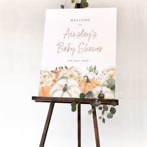 Op de afbeelding: Welkom bij Ainsley's Baby Shower bord met een aquarel-illustratie van pompoenen en bloemen. Het bord staat op een houten ezel en de datum is 3 juni 2020.