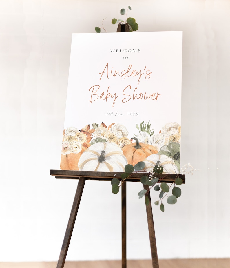Op de afbeelding: Welkom bij Ainsley's Baby Shower bord met een aquarel-illustratie van pompoenen en bloemen. Het bord staat op een houten ezel en de datum is 3 juni 2020.