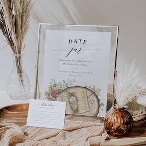 May include: A white card with the text "date ideas" and lines for writing. The card is in front of a framed sign with the text "DATE jar Share your best date ideas for the future Mr. & Mrs. LAUREN'S BRIDAL SHOWER 18th August 20xx".