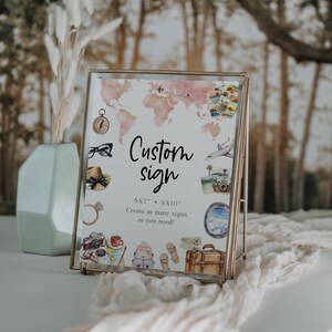 May include: A framed custom sign with a world map and travel-themed illustrations. The sign includes the text "Custom sign" and size options of 5x7 and 8x10 inches. The sign is in a gold frame.