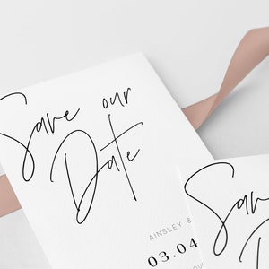 May include: Save the Date card with a handwritten script font. The card is white with a pink ribbon on top. The date is 03.04 and the names Ainsley & are printed below the date.