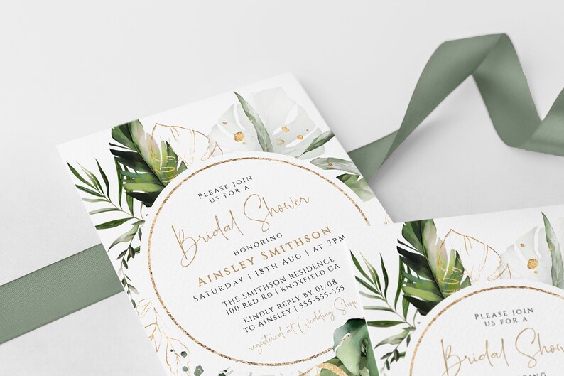 Op de afbeelding: Een witte kaart met gouden rand en groene aquarelbladeren. De tekst op de kaart luidt "U bent van harte welkom voor een Bridal Shower ter ere van Ainsley Smithson Zaterdag 18 augustus om 14:00 uur The Smithson Residence 100 Red Rd Knoxfield CA Graag uw antwoord v&oacute;&oacute;r 01/08 aan Ainsley op 555-555-555 geregistreerd bij Wedding Shop"
