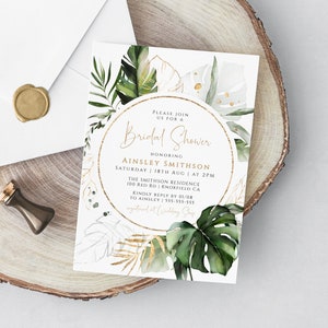 Op de afbeelding: Een witte uitnodiging met gouden accenten en groene tropische bladeren. De tekst luidt: "U bent van harte welkom voor een Bridal Shower ter ere van Ainsley Smithson Zaterdag 18 augustus om 14:00 uur The Smithson Residence 100 Red Rd Knoxfield CA Graag uw antwoord v&oacute;&oacute;r 01/08 aan Ainsley 555-555-555 geregistreerd bij Wedding Shop"