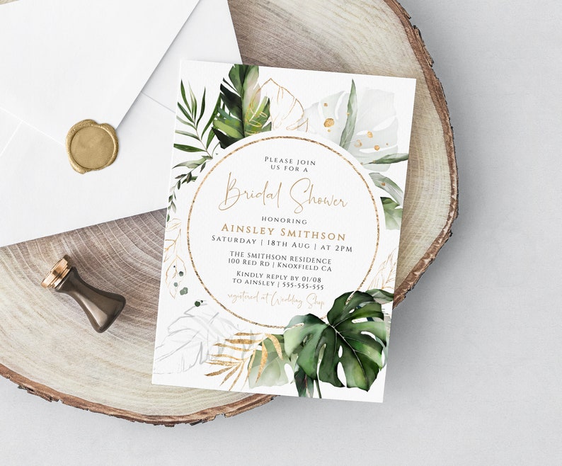 Op de afbeelding: Een witte uitnodiging met gouden accenten en groene tropische bladeren. De tekst luidt: "U bent van harte welkom voor een Bridal Shower ter ere van Ainsley Smithson Zaterdag 18 augustus om 14:00 uur The Smithson Residence 100 Red Rd Knoxfield CA Graag uw antwoord v&oacute;&oacute;r 01/08 aan Ainsley 555-555-555 geregistreerd bij Wedding Shop"