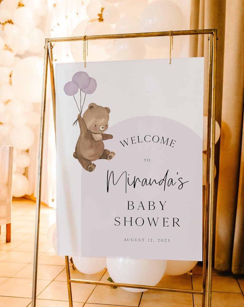 Puede incluir: Un cartel de bienvenida para un baby shower con un oso de dibujos animados sosteniendo globos morados. El cartel dice "Bienvenido a Miranda's Baby Shower 12 de agosto de 2023".
