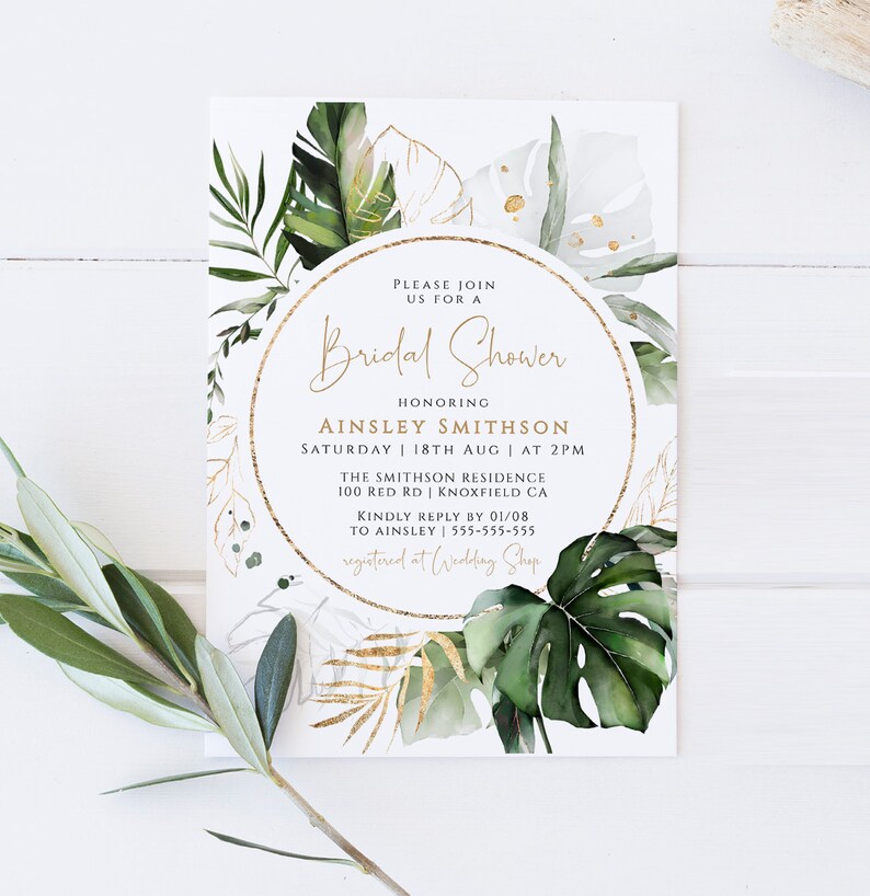 Op de afbeelding: Een witte kaart met een gouden cirkelrand en groene tropische bladeren. De tekst luidt "U bent van harte welkom op een Bridal Shower ter ere van Ainsley Smithson Zaterdag 18 augustus | om 14:00 uur The Smithson Residence 100 Red Rd | Knoxfield CA Graag uw antwoord v&oacute;&oacute;r 01/08 aan Ainsley | 555-555-555 Geregistreerd bij Wedding Shop"