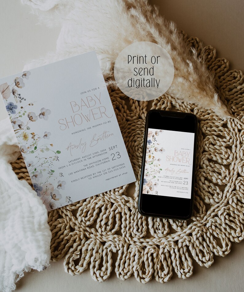 May include: A baby shower invitation with a floral design in shades of blue and white. The invitation is printed on a white background and features the text "Join us for a Baby Shower" in a gold script font. The invitation also includes the date, time, and location of the shower. The invitation is displayed on a phone screen and a white surface.