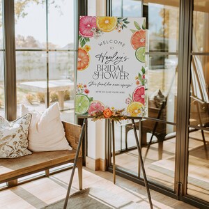 Puede incluir: Un cartel de bienvenida para una despedida de soltera con tem&aacute;tica c&iacute;trica. El cartel presenta una ilustraci&oacute;n de acuarela de limones, limas y naranjas con flores y vegetaci&oacute;n. El texto dice "Bienvenido a la despedida de soltera de Hayley. &iexcl;Encontr&oacute; a su alma gemela! &iexcl;Estamos encantados de que est&eacute;s aqu&iacute;!"