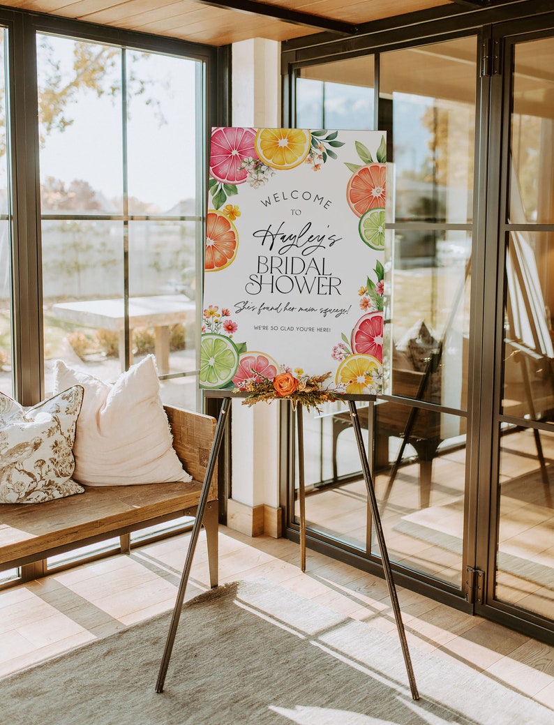 Puede incluir: Un cartel de bienvenida para una despedida de soltera con tem&aacute;tica c&iacute;trica. El cartel presenta una ilustraci&oacute;n de acuarela de limones, limas y naranjas con flores y vegetaci&oacute;n. El texto dice "Bienvenido a la despedida de soltera de Hayley. &iexcl;Encontr&oacute; a su alma gemela! &iexcl;Estamos encantados de que est&eacute;s aqu&iacute;!"