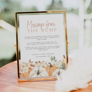 May include: A white card with a gold frame and a message from the bump. The card has a watercolour illustration of pumpkins and flowers. The text reads: "Message from the bump. Thank you for being here for my mommy. It won't be long now till I come out of her tummy. I can't be there to thank you all, but I know my mommy loves you all! I know you all can't wait until I'm here, so make some memories today and hold them dear! Ainsley's Baby Shower 3rd September 2021."