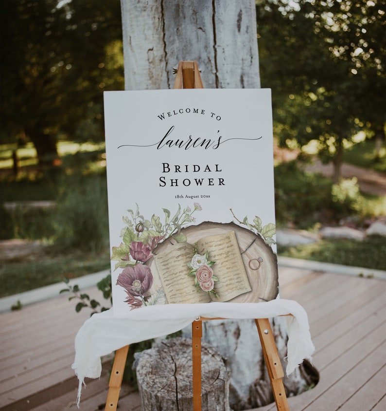 May include: A white sign with the text "Welcome to Lauren's Bridal Shower 18th August 20xx" and a watercolor illustration of an open book with flowers and a ring on a tree stump.