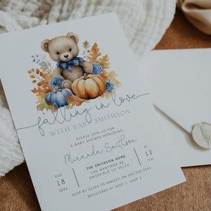 May include: A baby shower invitation featuring a watercolour illustration of a teddy bear holding a pumpkin, surrounded by autumn leaves and blue flowers. The text reads "falling in love with baby Smithson".