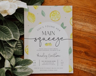 Pode incluir: Um convite para um chá de panela com tema de limão com ilustrações de aquarela de limões e folhas. O convite diz "She's found her main squeeze" e inclui o nome da noiva, Ainsley Smithson, a data e hora do chá de panela, e o local. Também inclui informações de RSVP.