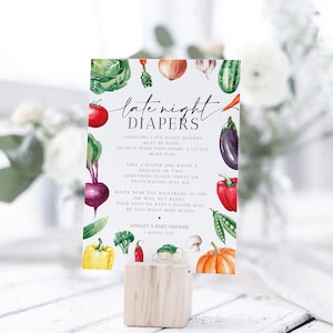 Op de afbeelding: Een babyborrelbord met aquarel illustraties van groenten, waaronder tomaten, bieten en pompoenen. Op het bord staat "late night luiers" en het geeft instructies voor het verschonen van luiers. Het bord wordt weergegeven op een houten blok.