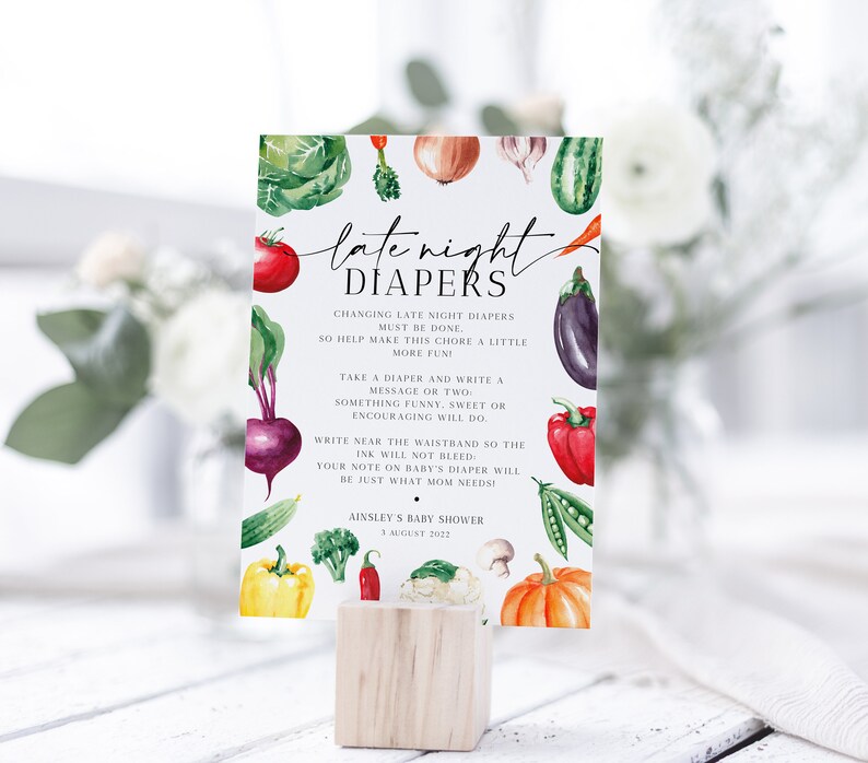 Op de afbeelding: Een babyborrelbord met aquarel illustraties van groenten, waaronder tomaten, bieten en pompoenen. Op het bord staat "late night luiers" en het geeft instructies voor het verschonen van luiers. Het bord wordt weergegeven op een houten blok.