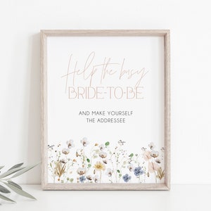 May include: A printable sign with the text "Help the busy bride-to-be and make yourself the addressee" in a light brown font. The sign is decorated with a border of watercolor flowers in shades of white, blue, yellow, and pink.