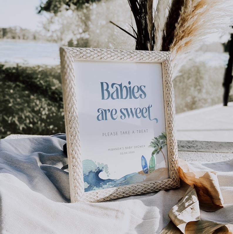 May include: A white framed sign with the text "Babies are sweet" in blue. The sign also includes the text "Please take a treat" and "Miranda's Baby Shower 03.04.20XX". The sign has a watercolor illustration of a wave, surfboards, and a palm tree.