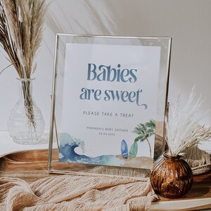 May include: A framed sign with a blue watercolor background and the text "Babies are sweet" in blue. The sign also includes a palm tree, waves, and surfboards. The text "Please take a treat" is below the main text, and the text "Miranda's Baby Shower 03.04.20XX" is below that.