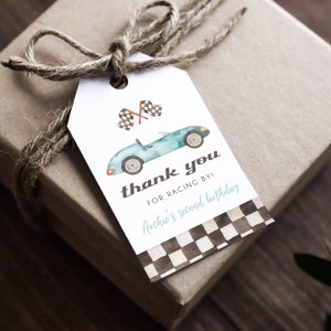 May include: A gift tag with a watercolor illustration of a blue race car and checkered flags. The tag reads "thank you for racing by!" and "Archie's second birthday" on a white background with a checkered pattern.