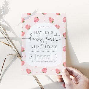 Op de afbeelding: Een roze en witte uitnodiging met een aardbeienpatroon. De uitnodiging luidt "Doe mee met Hayleys eerste verjaardag, een bessenfeest" met de datum en tijd van het feest. RSVP-informatie is onderaan opgenomen.