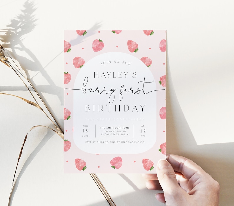 Op de afbeelding: Een roze en witte uitnodiging met een aardbeienpatroon. De uitnodiging luidt "Doe mee met Hayleys eerste verjaardag, een bessenfeest" met de datum en tijd van het feest. RSVP-informatie is onderaan opgenomen.