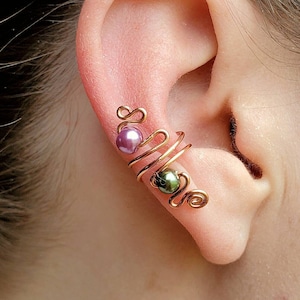 May include: A gold ear cuff with a spiral design and two small beads, one purple and one green.