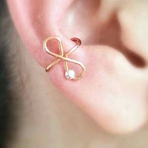 May include: Gold ear cuff with a small clear rhinestone. The ear cuff is shaped like an infinity symbol.