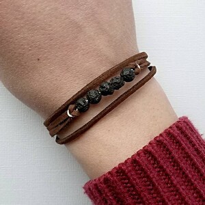 May include: A brown leather wrap bracelet with black lava rock beads. The bracelet is worn on a person's wrist.