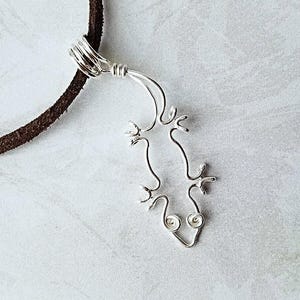 May include: A silver wire gecko pendant necklace on a brown leather cord.