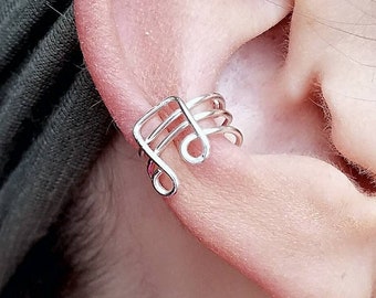 May include: A silver ear cuff shaped like a treble clef. The cuff is worn on the upper part of the ear, just above the cartilage.