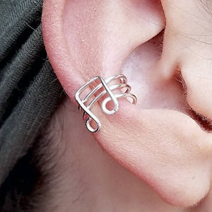 May include: A silver ear cuff shaped like a treble clef. The cuff is worn on the upper part of the ear, just above the cartilage.