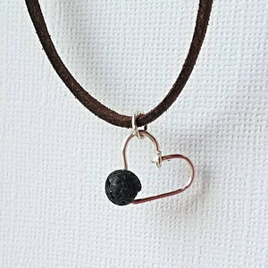 May include: A brown suede cord necklace with a silver heart charm and a black lava rock bead.