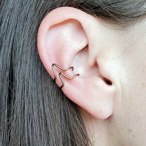 May include: A pair of gold ear cuffs in the shape of a star. The cuffs are worn on the upper part of the ear, just above the cartilage.