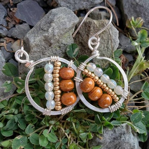 May include: Silver hoop earrings with wooden beads, iridescent glass beads, and gold beads. The earrings are hanging from silver hooks.